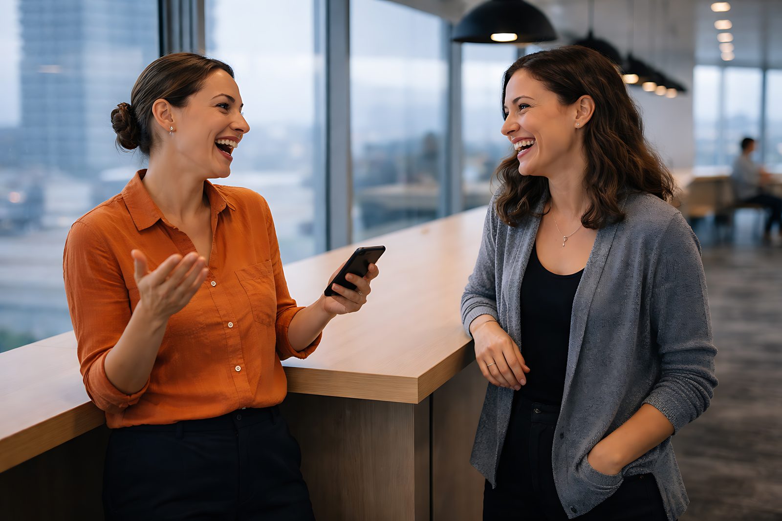 Two colleagues laughing together in a bright modern office